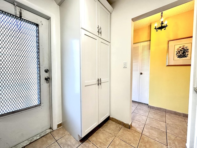 corridor featuring light tile patterned floors, baseboards, and a chandelier