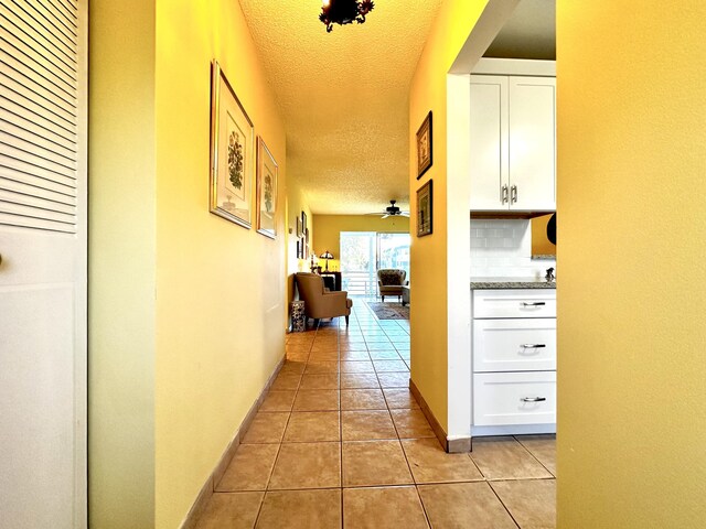 hallway with light tile patterned flooring, baseboards, and a textured ceiling