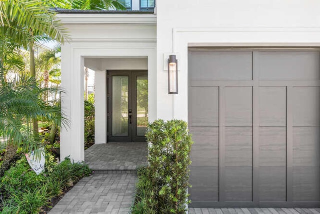 view of exterior entry featuring stucco siding, french doors, and a garage