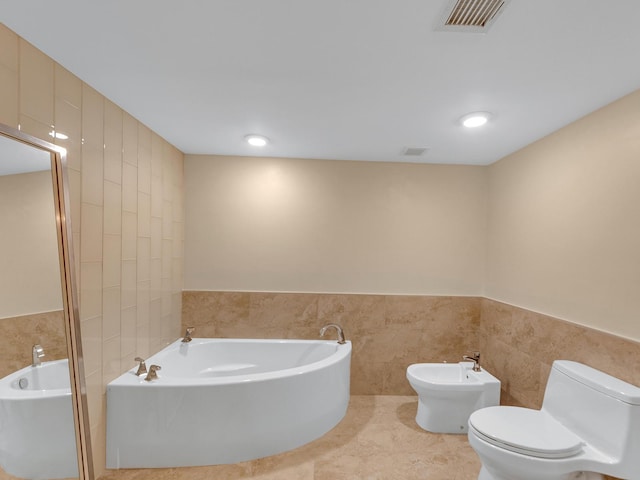 bathroom featuring visible vents, toilet, a bidet, a garden tub, and tile walls