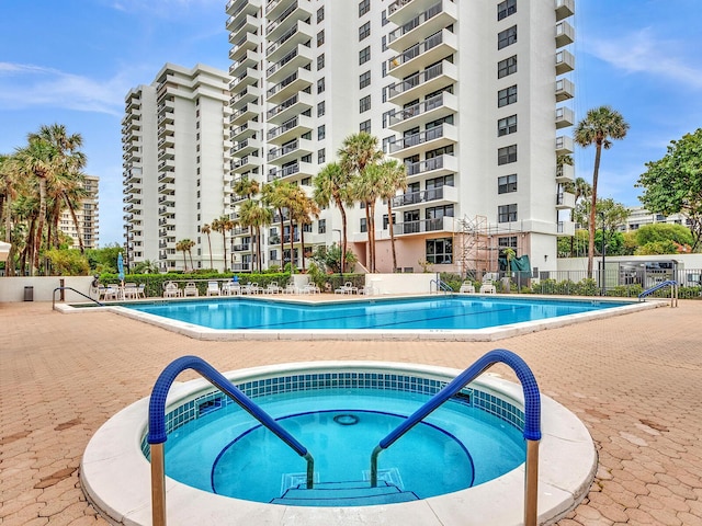 community pool with a patio area, fence, and a hot tub