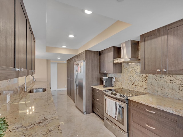 kitchen featuring a sink, tasteful backsplash, stainless steel appliances, wall chimney range hood, and light stone countertops