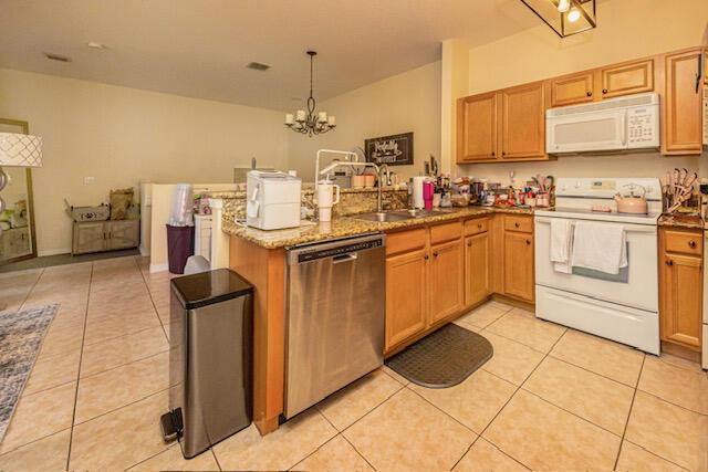 kitchen featuring light tile patterned flooring, white appliances, a peninsula, and a sink