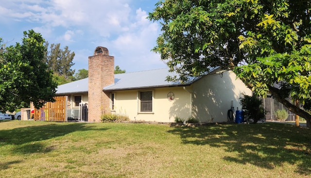 back of property with a lawn, metal roof, and stucco siding