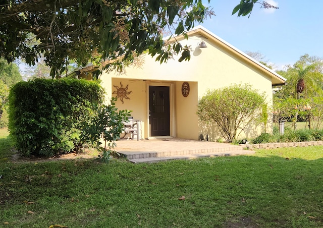 property entrance featuring stucco siding, a patio, and a lawn