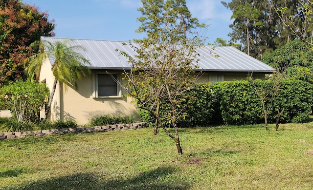 view of side of property featuring stucco siding, a yard, and metal roof