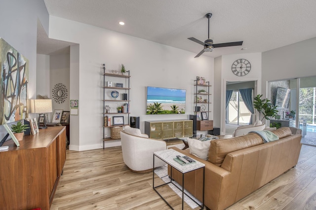 living room featuring ceiling fan, light wood-style floors, baseboards, and a textured ceiling