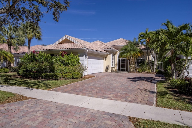 mediterranean / spanish home featuring a garage, decorative driveway, stucco siding, and a tile roof