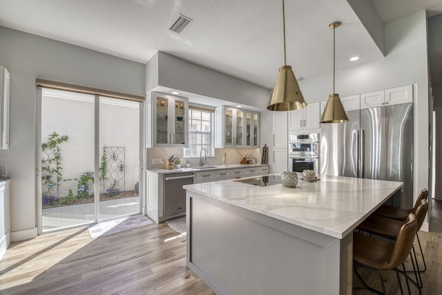 kitchen with a kitchen island, light stone countertops, light wood-type flooring, stainless steel appliances, and a sink