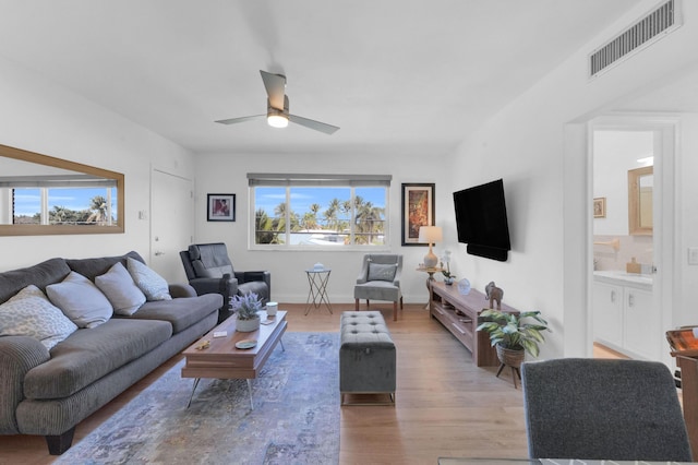 living area with visible vents, light wood-style flooring, baseboards, and a ceiling fan