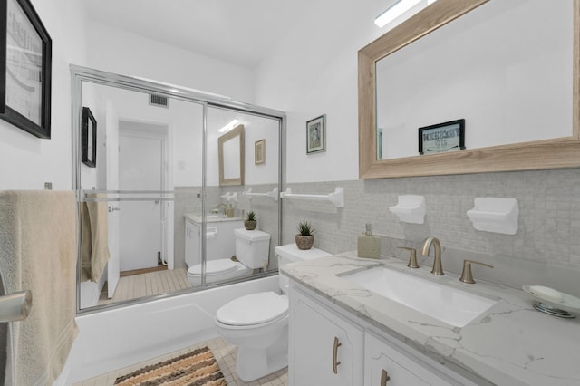 bathroom with visible vents, tile walls, bath / shower combo with glass door, toilet, and vanity