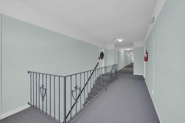 corridor featuring baseboards, an upstairs landing, and carpet flooring