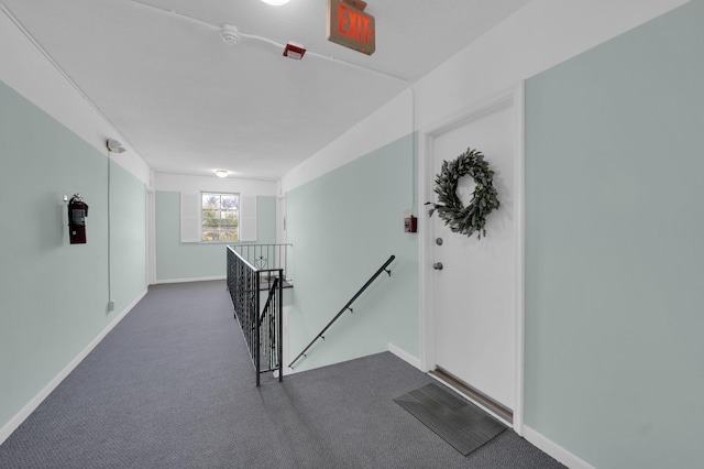 hallway with an upstairs landing, baseboards, and carpet