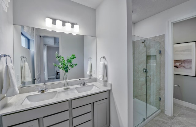 full bathroom with a textured ceiling, a shower stall, double vanity, and a sink