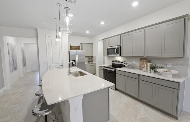 kitchen with a kitchen bar, an island with sink, gray cabinets, a sink, and appliances with stainless steel finishes