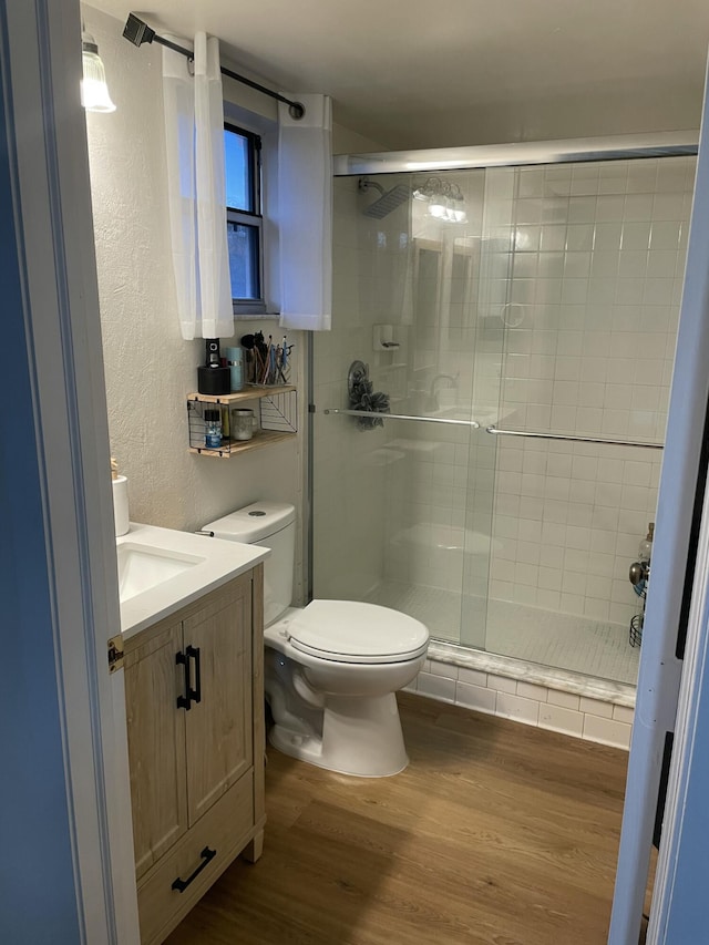 bathroom with toilet, wood finished floors, a stall shower, and a textured wall