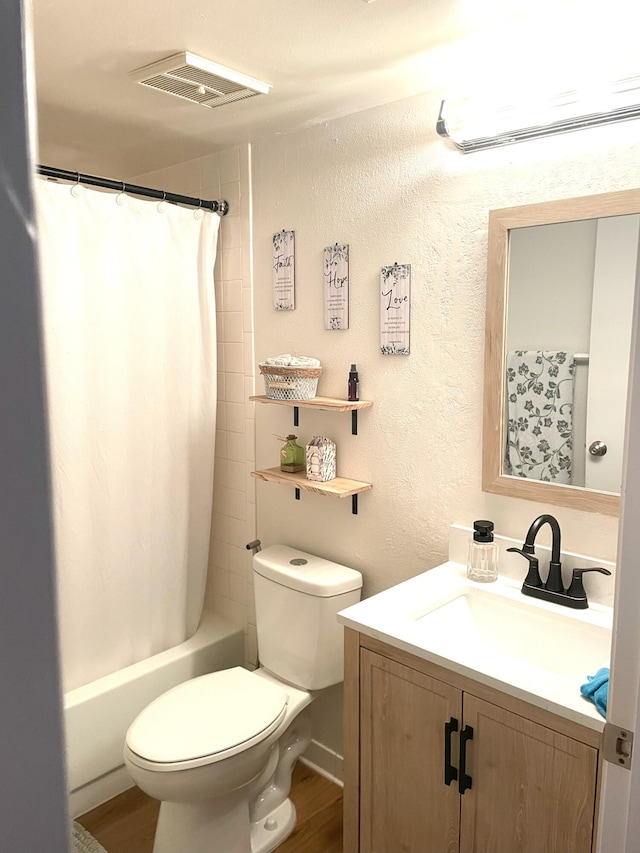 bathroom featuring visible vents, toilet, wood finished floors, vanity, and a textured wall