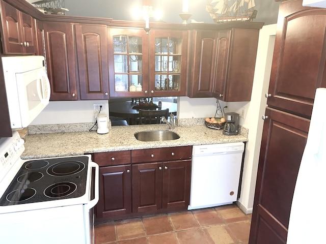 kitchen with white appliances, glass insert cabinets, light stone countertops, and a sink