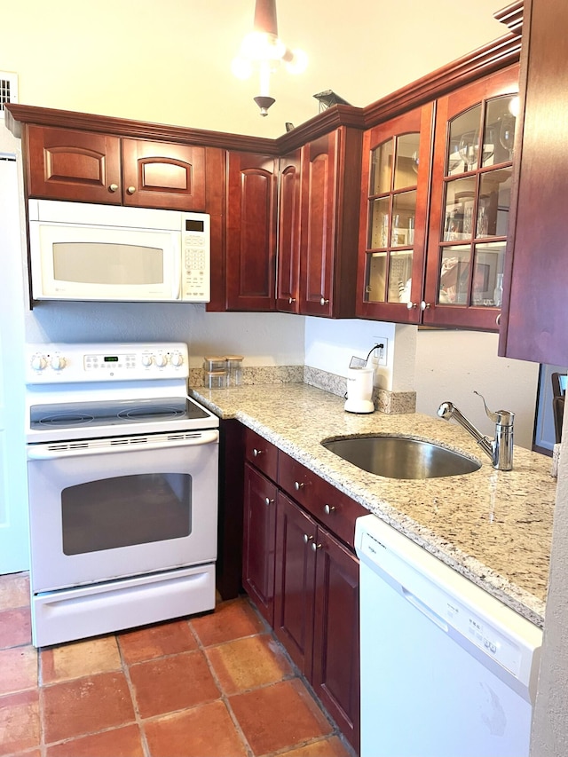 kitchen featuring a sink, light stone counters, white appliances, reddish brown cabinets, and glass insert cabinets