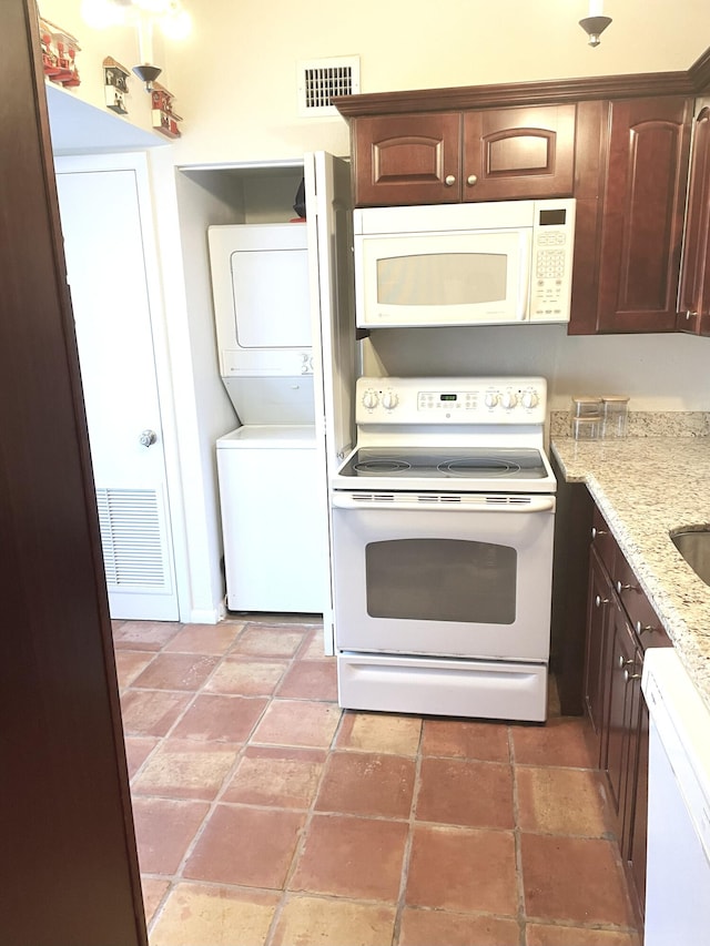 kitchen with dark brown cabinetry, stacked washer / dryer, white appliances, and visible vents