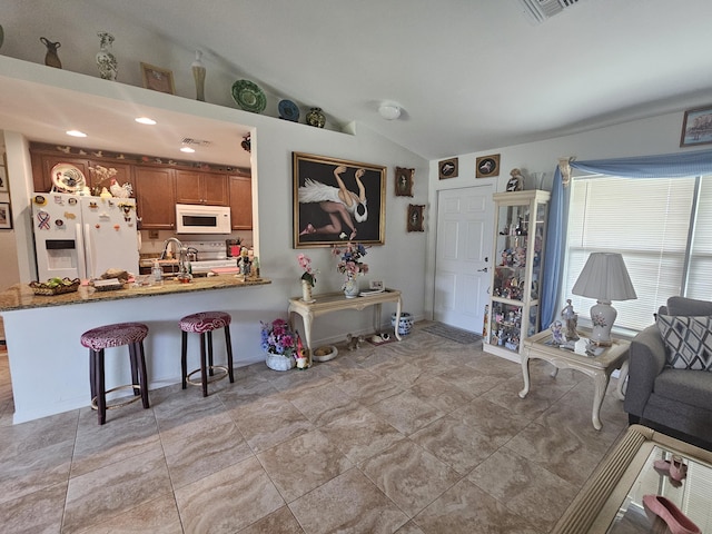 kitchen with vaulted ceiling, brown cabinets, a kitchen breakfast bar, a peninsula, and white appliances