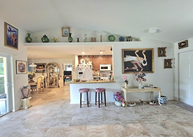 kitchen featuring white appliances, a breakfast bar, lofted ceiling, and a peninsula