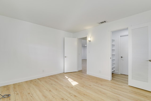 unfurnished bedroom with a spacious closet, visible vents, light wood-type flooring, and baseboards