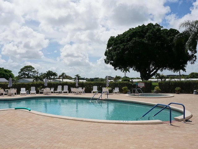 community pool featuring a patio, fence, and a hot tub