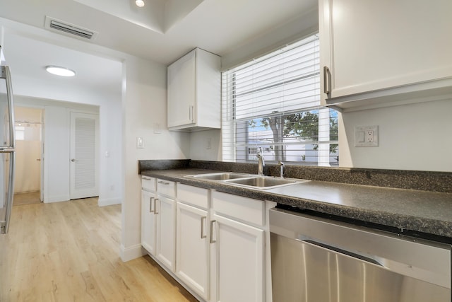 kitchen featuring dishwasher, a sink, dark countertops, white cabinetry, and light wood-type flooring