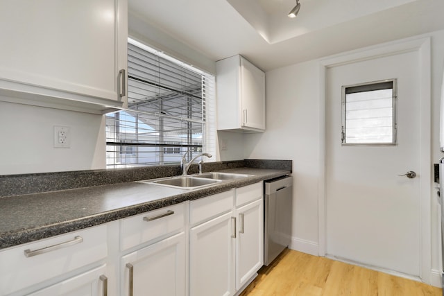 kitchen with a sink, dishwasher, light wood finished floors, white cabinetry, and dark countertops