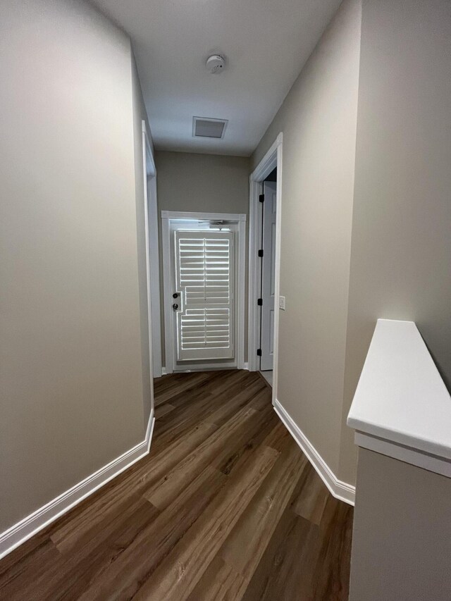 hall with visible vents, baseboards, and dark wood-style flooring