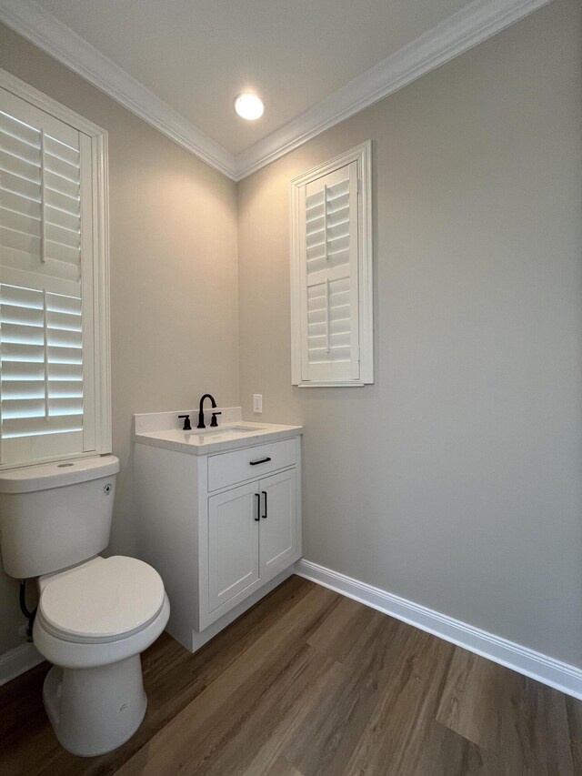 bathroom featuring vanity, wood finished floors, baseboards, ornamental molding, and toilet