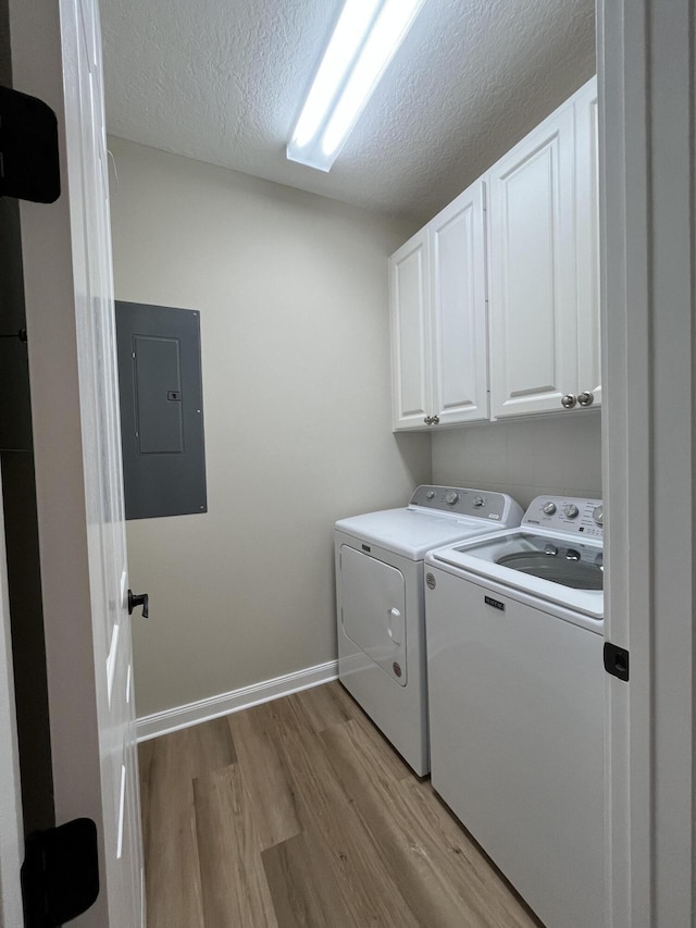 laundry room featuring light wood finished floors, electric panel, cabinet space, a textured ceiling, and washer and dryer