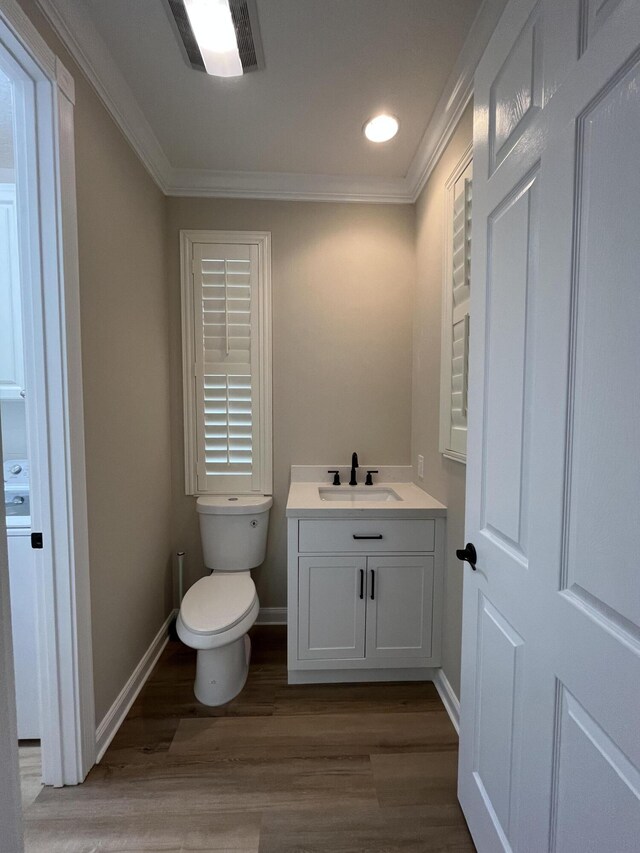 bathroom featuring toilet, wood finished floors, vanity, and ornamental molding