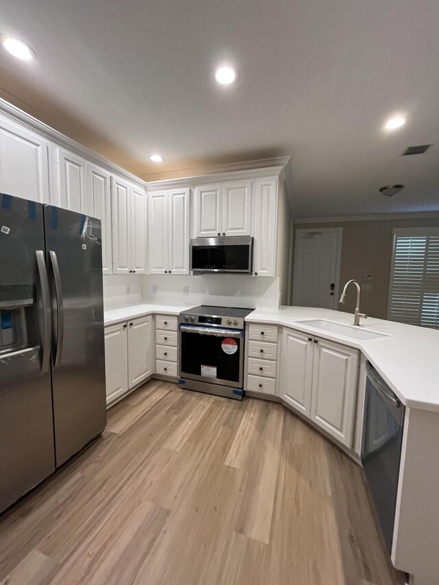 kitchen featuring a sink, light wood-style floors, appliances with stainless steel finishes, a peninsula, and light countertops