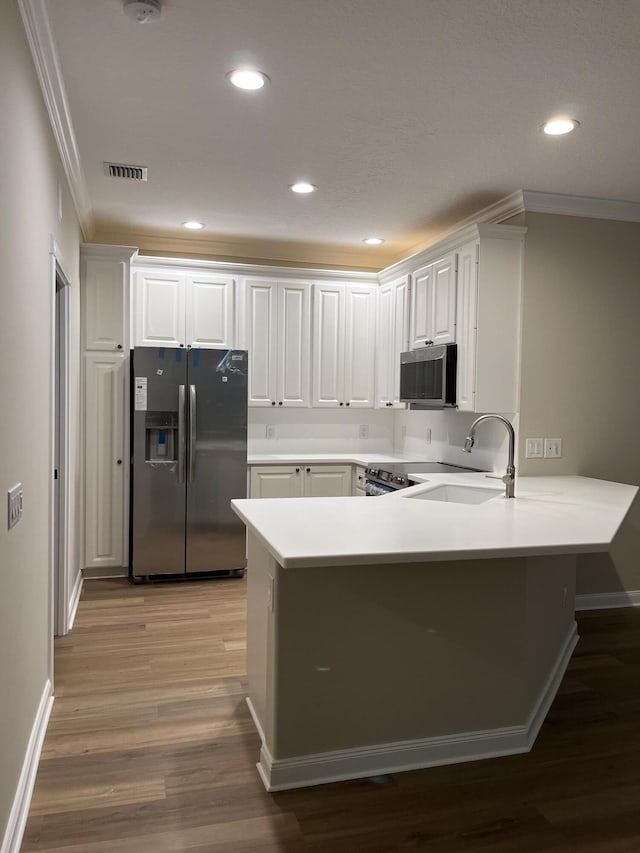 kitchen featuring visible vents, appliances with stainless steel finishes, a peninsula, wood finished floors, and a sink