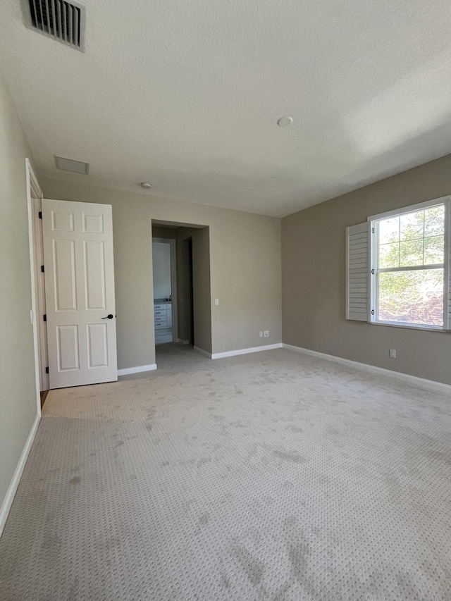 empty room with visible vents, light colored carpet, a textured ceiling, and baseboards