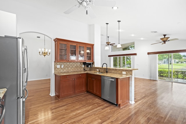 kitchen with brown cabinets, a sink, arched walkways, appliances with stainless steel finishes, and a peninsula