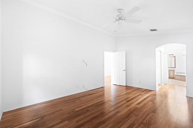 spare room with arched walkways, wood finished floors, a ceiling fan, and ornamental molding