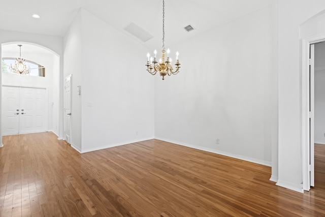 interior space with a notable chandelier, wood finished floors, arched walkways, and baseboards