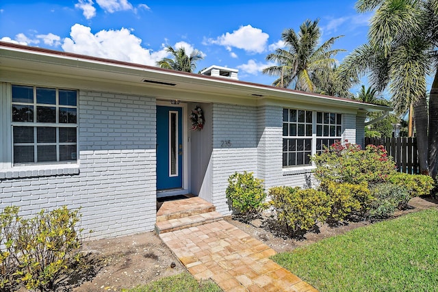 view of exterior entry featuring brick siding and fence