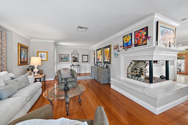 living room with a fireplace with raised hearth, wood finished floors, visible vents, and ornamental molding