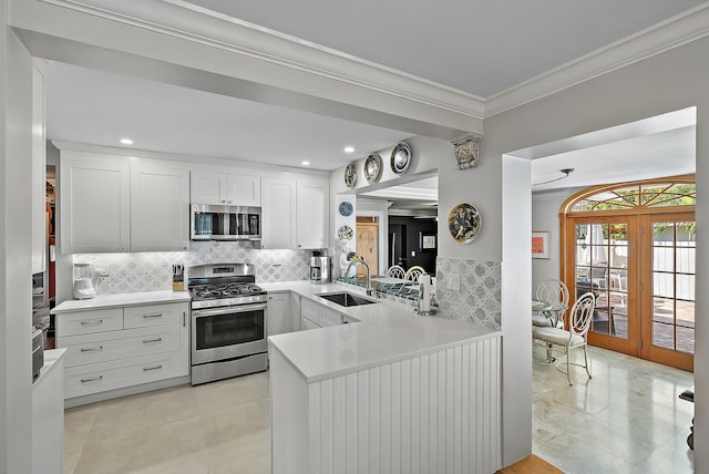 kitchen with ornamental molding, a sink, backsplash, stainless steel appliances, and a peninsula