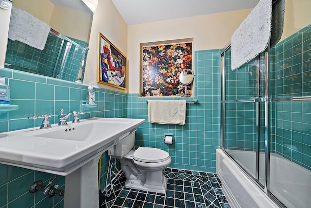 full bath with a wainscoted wall, shower / bath combination with glass door, tile patterned floors, toilet, and tile walls