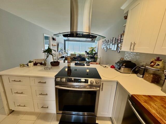 kitchen with stainless steel range with electric stovetop, island exhaust hood, white cabinetry, light countertops, and light tile patterned floors