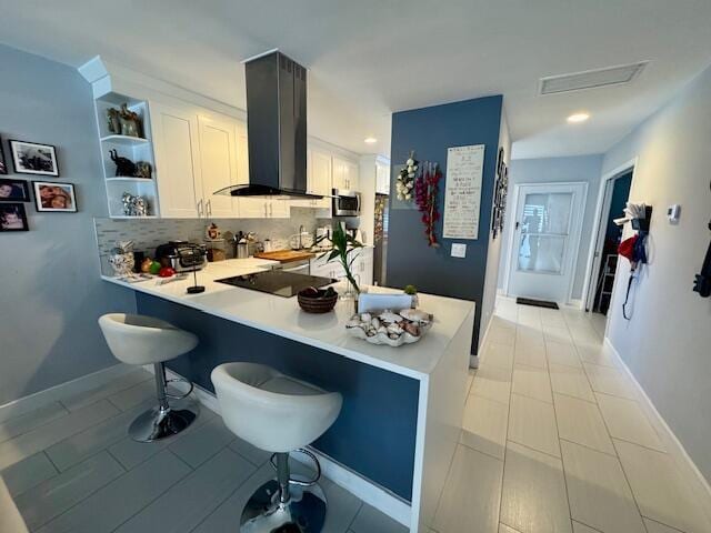 kitchen featuring a kitchen bar, open shelves, stainless steel microwave, a peninsula, and exhaust hood