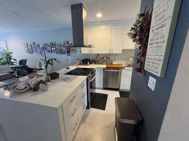 kitchen with island exhaust hood, stainless steel appliances, a peninsula, and white cabinetry