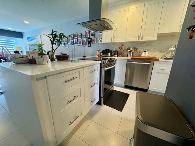 kitchen featuring appliances with stainless steel finishes, white cabinetry, light countertops, and wall chimney range hood