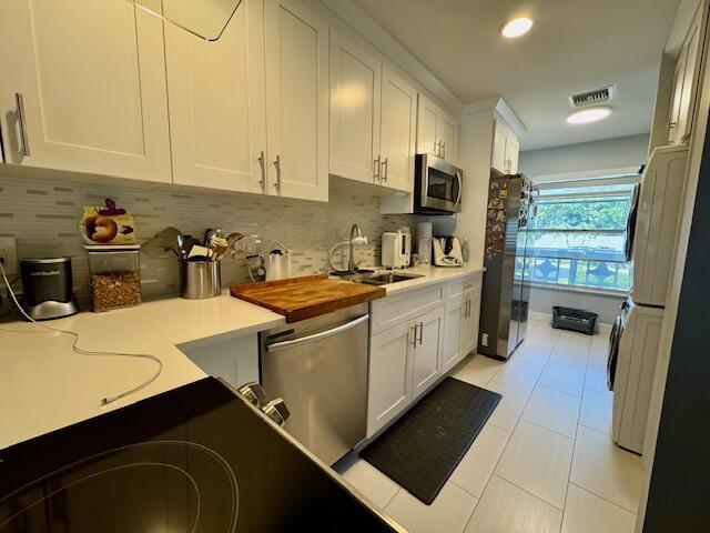 kitchen with visible vents, a sink, stainless steel appliances, white cabinets, and decorative backsplash