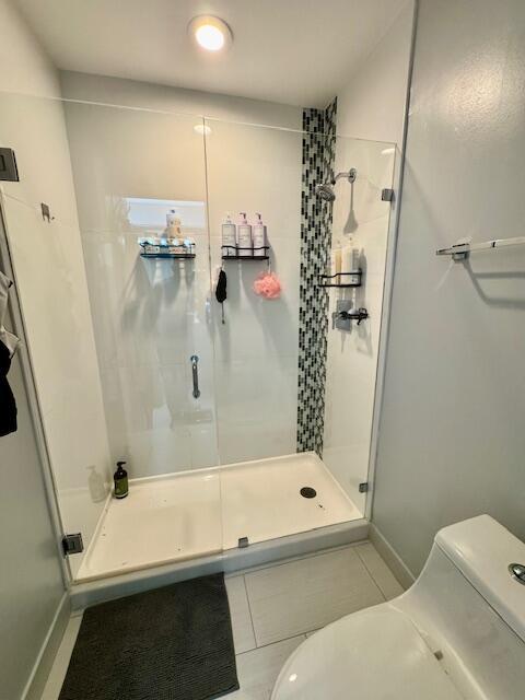 full bath featuring tile patterned flooring, a shower stall, toilet, and baseboards